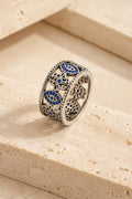 Cetara Evil Eye Ring on warm travertine stone, carved eye and hamsa band set with blue crystals