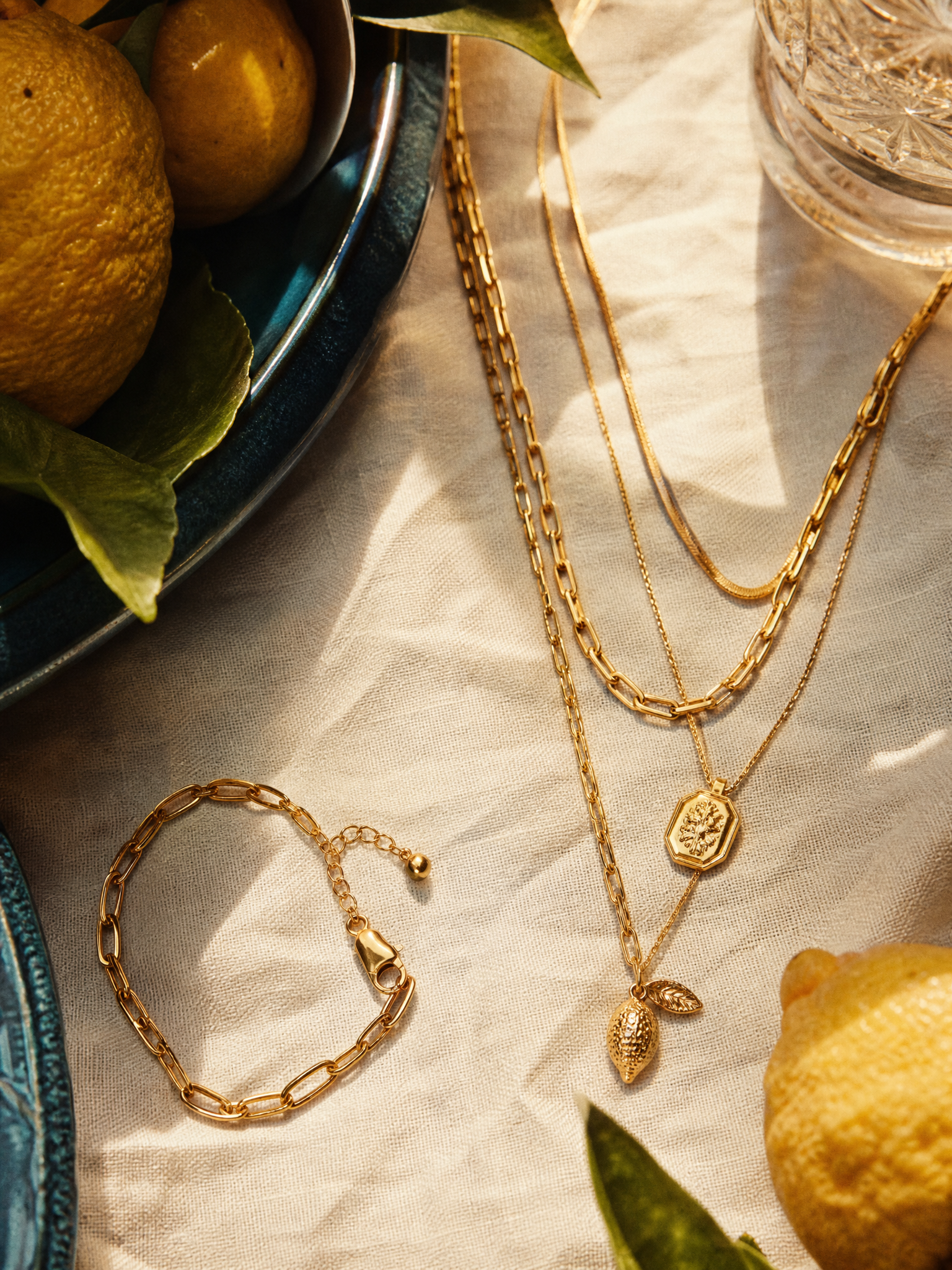 Layered gold necklaces and a bracelet on cream linen with lemons