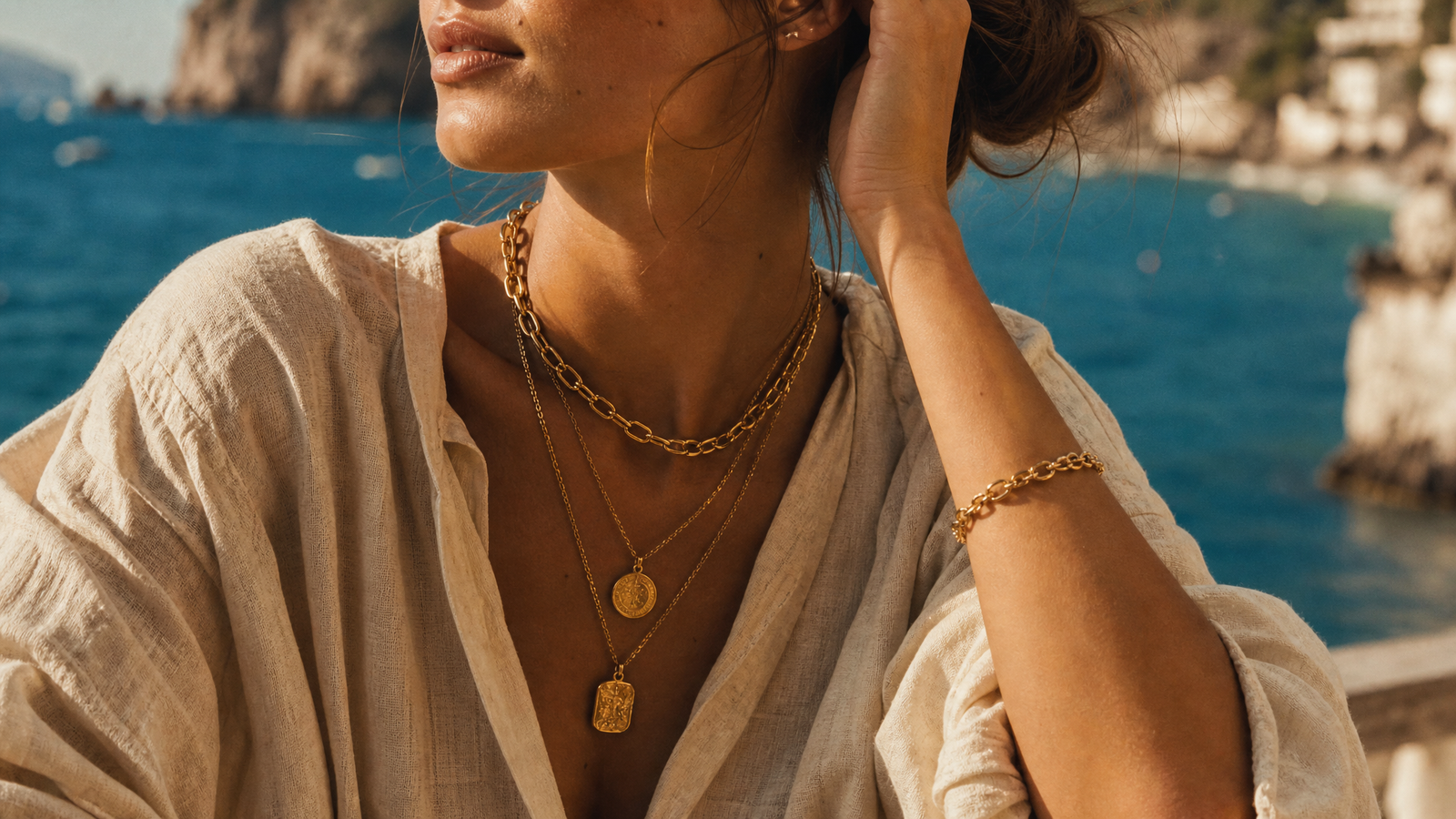 Layered gold jewelry on cream linen by the sea