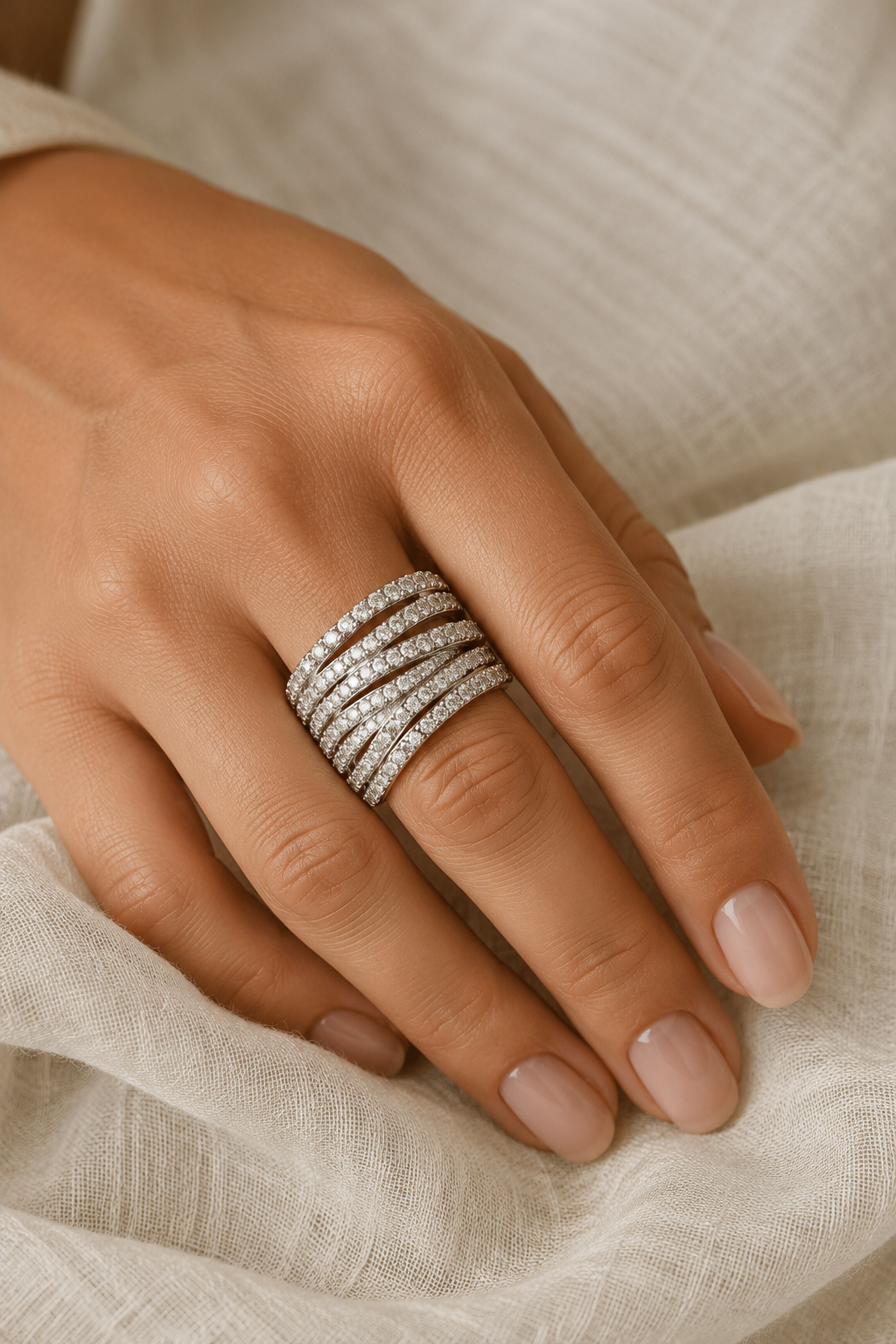 Close crop of a hand on cream linen wearing the wide Abbraccio pave crossover ring