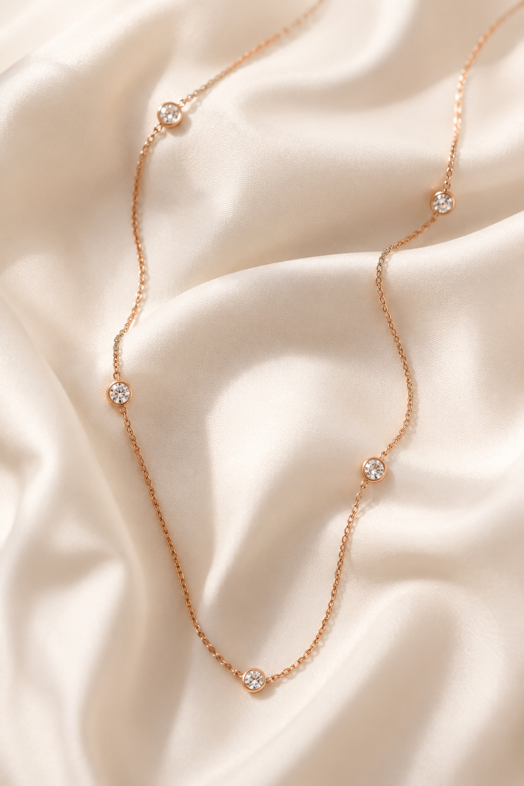 Stellina station necklace in rose gold arranged on ivory silk