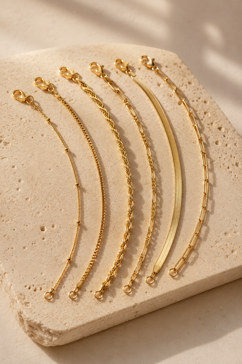 Sei six dainty gold chain bracelets on travertine