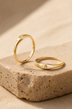 Lettera gold initial ring standing on travertine stone