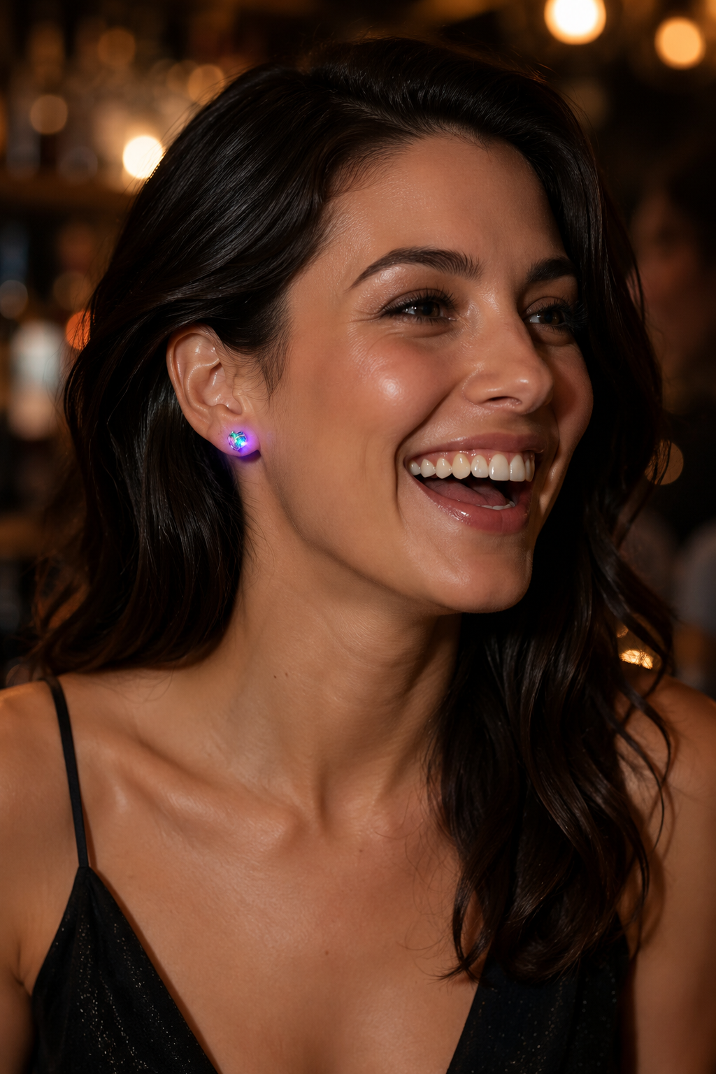 Woman laughing in a dark bar wearing a Lucciola LED stud glowing at her earlobe