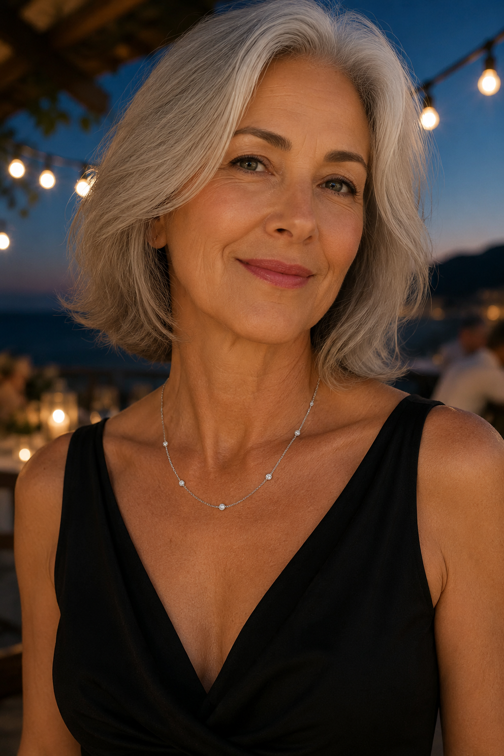Woman with silver-grey hair in a black evening top wearing the Stellina necklace in white gold at dusk