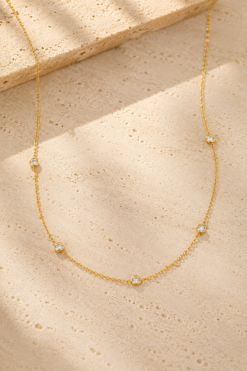 Stellina station necklace in yellow gold on warm travertine stone, five bezel-set crystals along a fine cable chain
