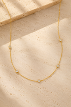 Stellina station necklace in yellow gold on warm travertine stone, five bezel-set crystals along a fine cable chain