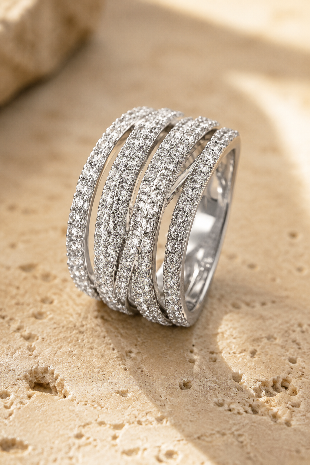 Abbraccio crossover ring standing on warm travertine stone, six pave-set bands crossing over one another
