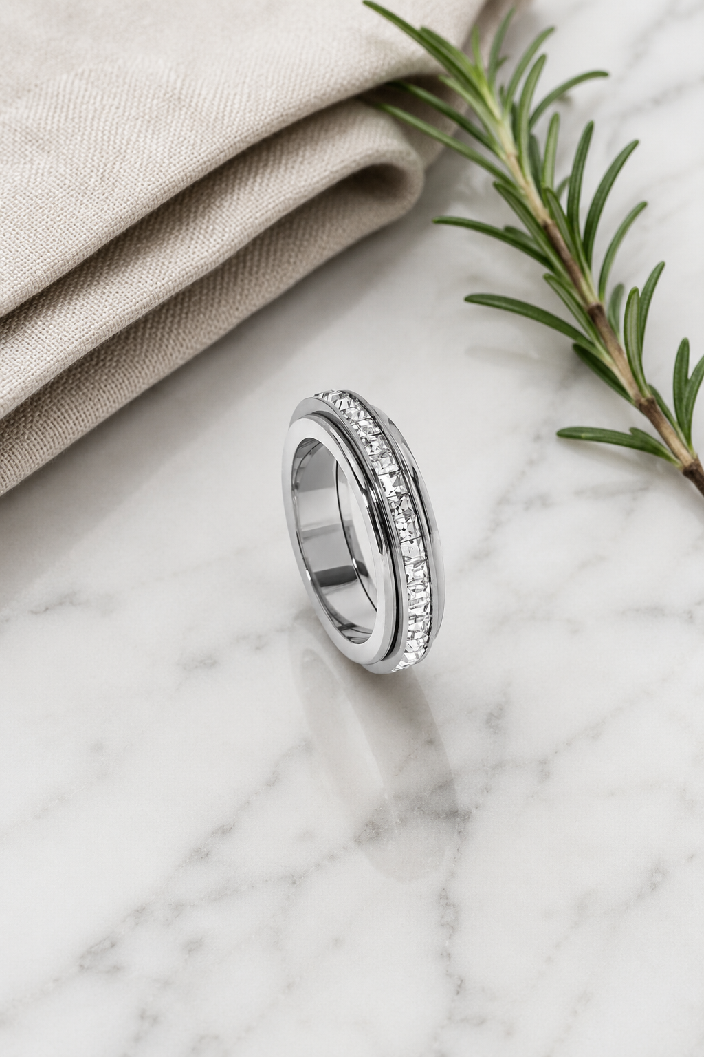 Silver Calma spinner ring flat-lay with rosemary