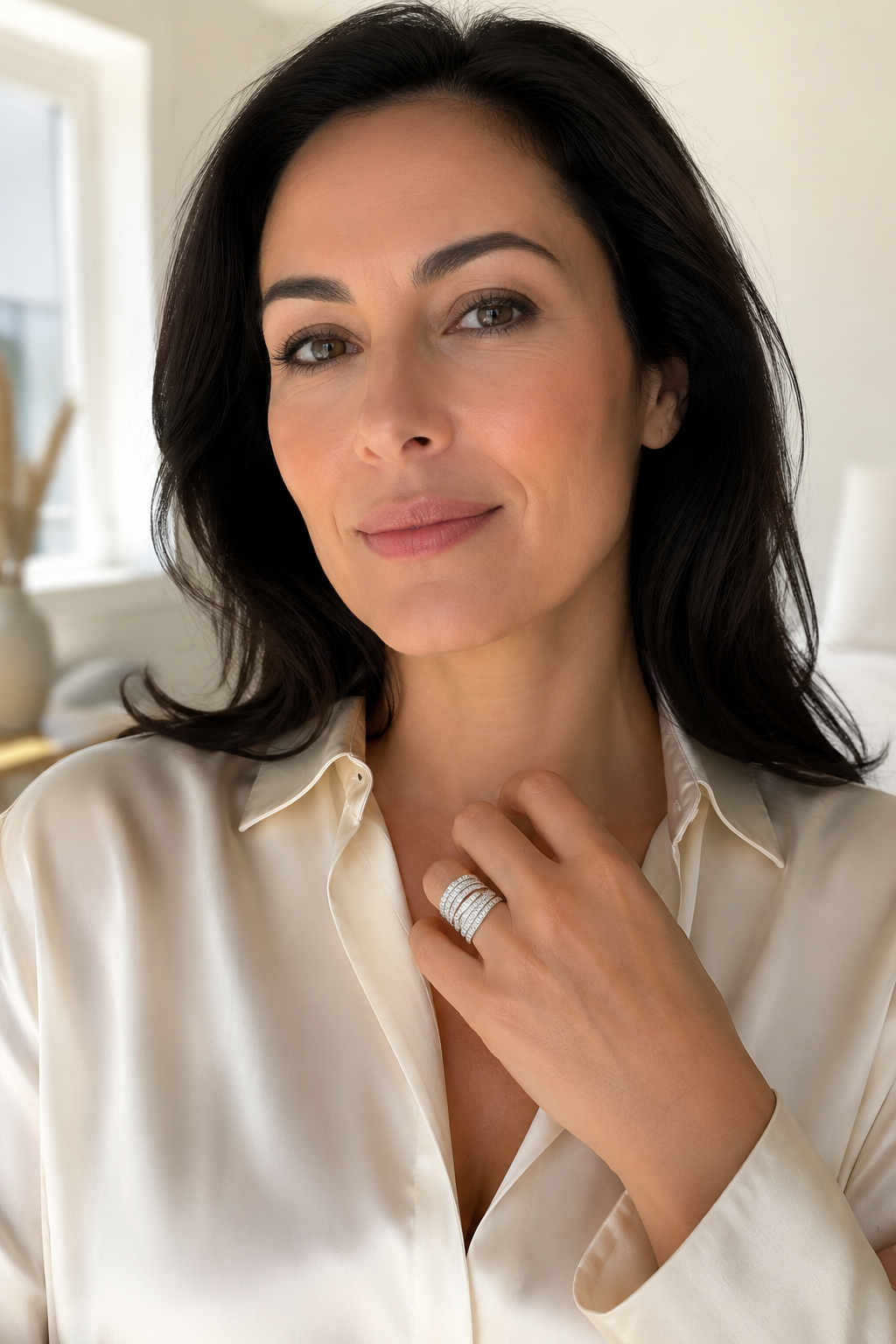 Woman in a cream silk blouse with her hand raised, wearing the Abbraccio crossover ring