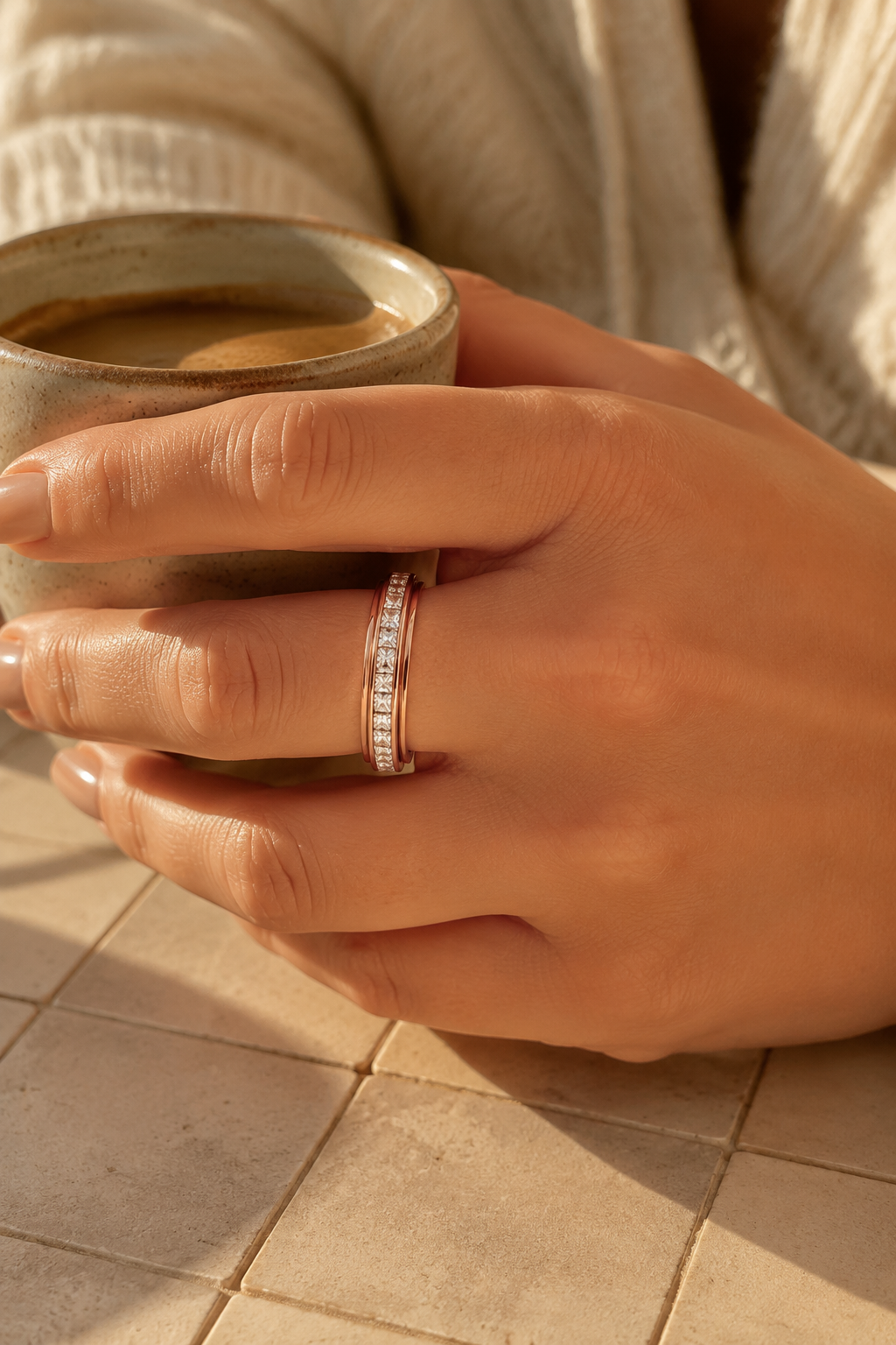 Rose gold Calma spinner ring on a hand holding an espresso cup