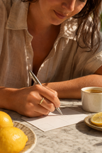 Woman writing a postcard wearing the Lettera initial ring