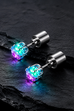 Pair of Lucciola LED stud earrings glowing cyan and magenta on dark slate, cylindrical steel backs visible