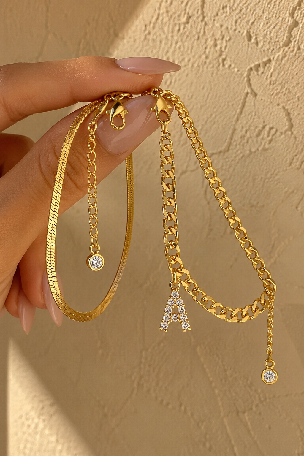 Marea anklet set held between fingertips against a plaster wall