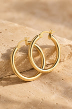 Ischia chunky gold tube hoop earrings on warm travertine stone