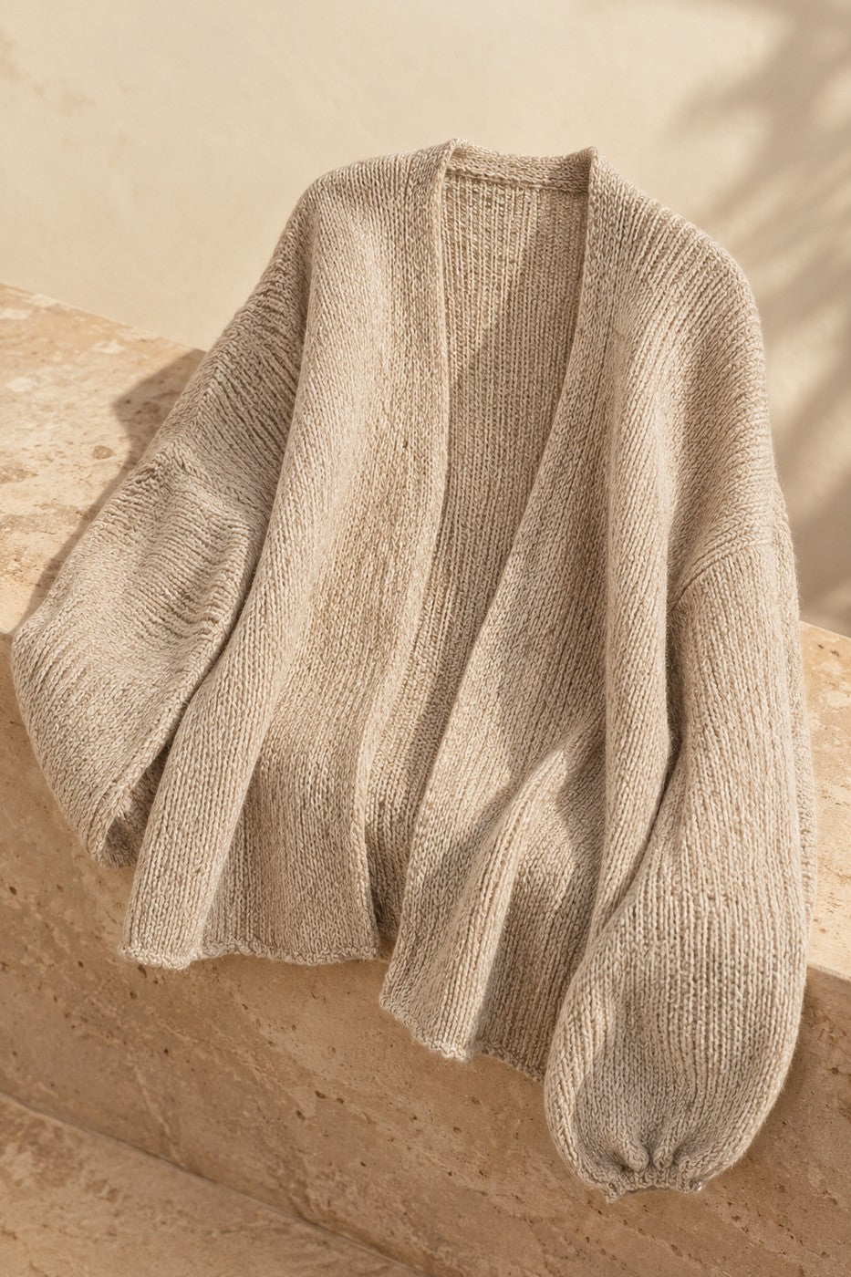 Nuvola oversized cardigan draped on warm travertine stone