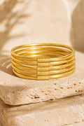 Quiete set of six soft-gold bangles on warm travertine stone
